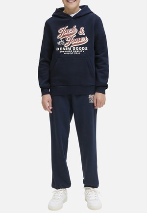 Sweatshirt marine avec capuche et poche frontale, arborant un texte graphique blanc et rouge, associé à un jogging marine assorti et des baskets blanches.