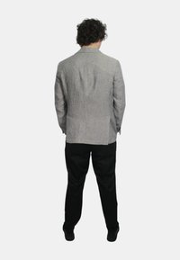 Blazer a righe grigio e bianco, caratterizzato da un taglio sartoriale con rever a scoprire, indossato sopra pantaloni neri, visto da dietro.