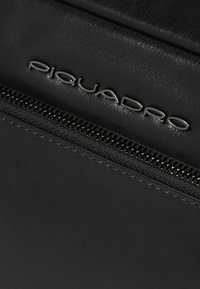 Zwart leren tas met een zilveren metalen rits en logo. De textuur is glad met een matte afwerking, die de details van het vakmanschap accentueert.