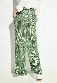 Gröna randiga vida byxor med ett vågigt mönster, med elastisk midja och sidfickor. Slätt tyg, avslappnad passform.