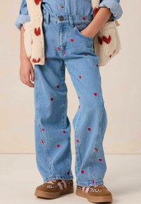 Jean en denim bleu avec broderie en forme de cœur rouge, coupe décontractée et taille haute. Associé à des sneakers à motifs marron et rose.