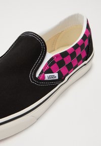 Botte noire à enfiler avec un motif à carreaux rose et noir sur le côté, des coutures blanches et une semelle en caoutchouc blanche.