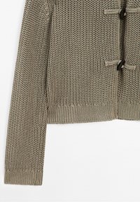 Pull beige en tricot à coupe courte, présentant un tissage texturé, un ourlet côtelé et deux fermetures à bascule noires.