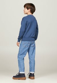 Felpa blu a maniche lunghe con orli e polsini a coste, abbinata a jeans larghi di un azzurro chiaro e stivali navy con suola marrone e logo.