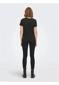 Camiseta de algodón negra de manga corta, con cuello redondo y un corte relajado, combinada con jeans ajustados negros y botines negros.