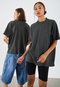 Oversized zwarte katoenen T-shirt met een ronde hals, gecombineerd met blauwe denim shorts en zwarte fiets shorts. Unisex ontwerp, relaxed fit.