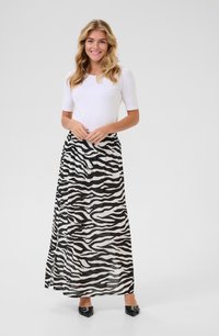 Jupe maxi avec un motif à rayures zèbre noir et blanc, en tissu léger, taille élastique et design fluide. Associée avec un haut ajusté blanc.