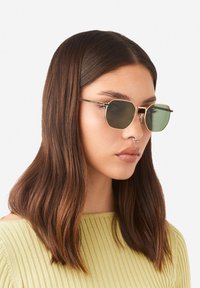 Asteiliste prillid rohelise tooniga läätsedega ja õhuke kuldne metallraam, millel on selged ninasilla padjad ja õhukesed mustad templivarred.