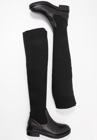 Botas negras por encima de la rodilla con puntera y tacón de cuero suave, caña de punto texturizada y puño acanalado. Tacón bajo tipo bloque.