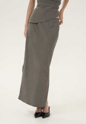 Gray fitted skirt with a high slit, made of smooth fabric. The design features a layered effect at the waist and is paired with black pointed shoes.