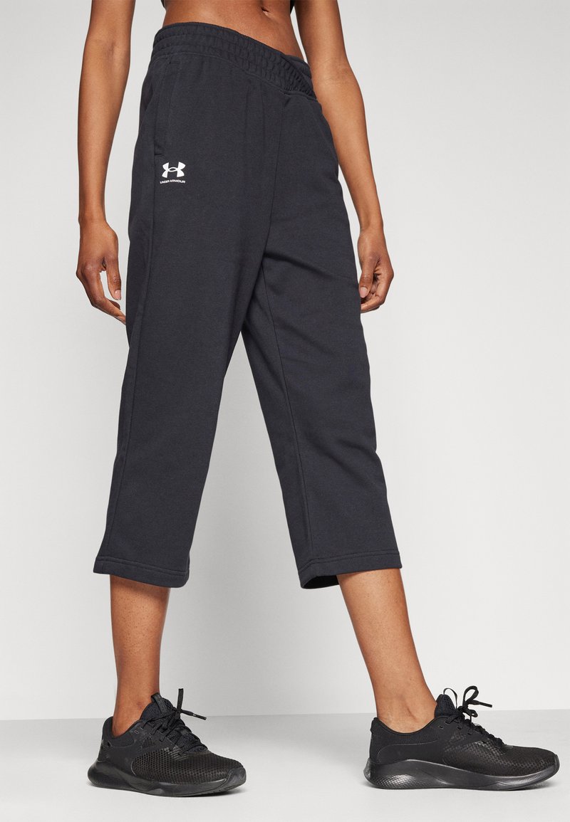 Černé zkrácené tepláky s elastickým pasem a bočními kapsami, s bílým logem Under Armour na levé noze.