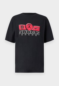 Μαύρο βαμβακερό μπλουζάκι με μεγάλο κόκκινο και λευκό γραφικό που απεικονίζει το κείμενο "Jordan Brand" και ένα εικονίδιο καλαθοσφαίρισης, κοντά μανίκια, στρογγυλή λαιμόκοψη.