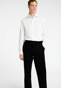 Bela srajca z dolgimi rokavi in klasičnim ovratnikom, kombinirana s črnimi žametnimi hlačami. Srajca ima gumbe vzdolž sprednje strani.