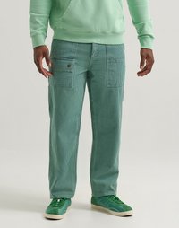 Mint green corduroy cargo pants with vertical stripes; features pockets at the sides; paired with matching green sneakers and a hoodie.