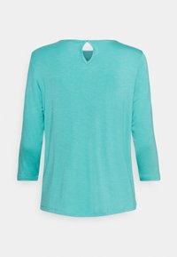 Turkos långärmad skjorta med en liten tårformad utskärning och knäppning vid baksidan av halsringningen.