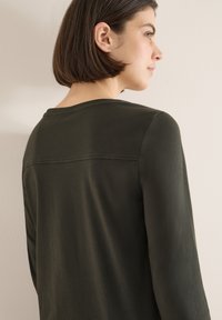 Dark green long-sleeve top made of smooth fabric, featuring a simple round neckline and a horizontal seam across the upper back.