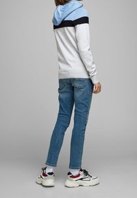 Felpa con cappuccio a righe blu chiaro e blu navy scuro, corpo grigio; abbinata a jeans blu e sneakers bianche chunky con dettagli rossi.