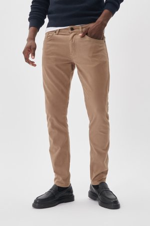 Pantalones ajustados en tono beige, con una textura suave. Cuentan con bolsillos frontales y cierre de botón. Combinados con mocasines negros.