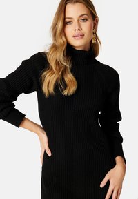 Maglione a collo alto nero con maniche lunghe e silhouette aderente. Tessuto texturizzato con una finitura liscia e un leggero stretch.