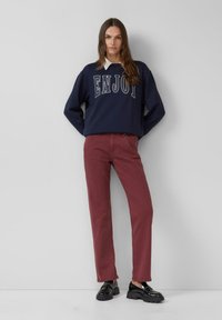 Tumesinine särk, millel on valge "NAUDI" tekst, koos burgundia sirge lõikega pükste ja mustade nurgeline põhi kingadega. Ühtsed värvid, mugav disain.