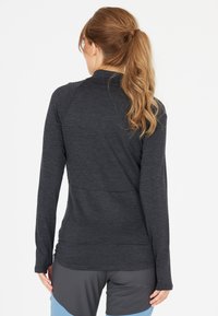 Langarm sporttop, donkergrijze textuurstof, aansluitend ontwerp, hoge kraag, gebogen zoom, gedragen met sportshorts.