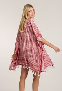 Sarkans un balts rakstains kaftans ar brīvu piegriezumu, izšūtām malām un atvērtām piedurknēm. Izgatavots no viegla materiāla, ar ģeometriskiem rakstiem.