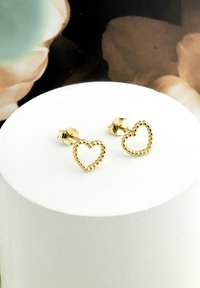 Orecchini a forma di cuore in oro con bordi perlati, caratterizzati da un design a perno. Posati su un semplice piedistallo bianco.
