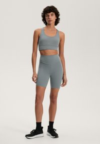 Grå sportbh och matchande högmidjade shorts, gjorda av stretchigt material med en jämn yta. Modellen bär svarta träningsskor.