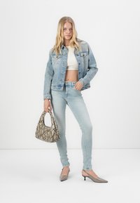 Svetle modrá džínsová bunda, bílý crop top, světlé džíny a šedé podpatky. Drží malou kabelku s hadím vzorem. Jednoduchý design s přiléhavým střihem.