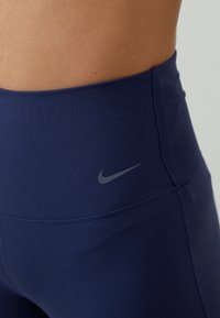 Morski visokovlečni leggins iz raztegljive tkanine, z diskretnim sivim logotipom Nike na boku. Šivi ustvarjajo prilagojen videz.