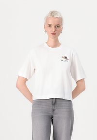 Hvit avkortet t-skjorte med korte ermer, prydet med en liten grafikk med teksten "BLAZING" og et designelement på brystet.