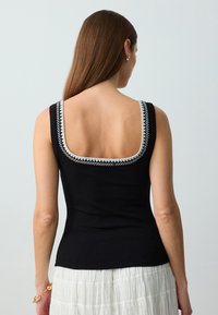 Top in cotone nero a costine con spalline larghe, scollo square e dettagli ricamati bianchi a contrasto lungo i bordi.