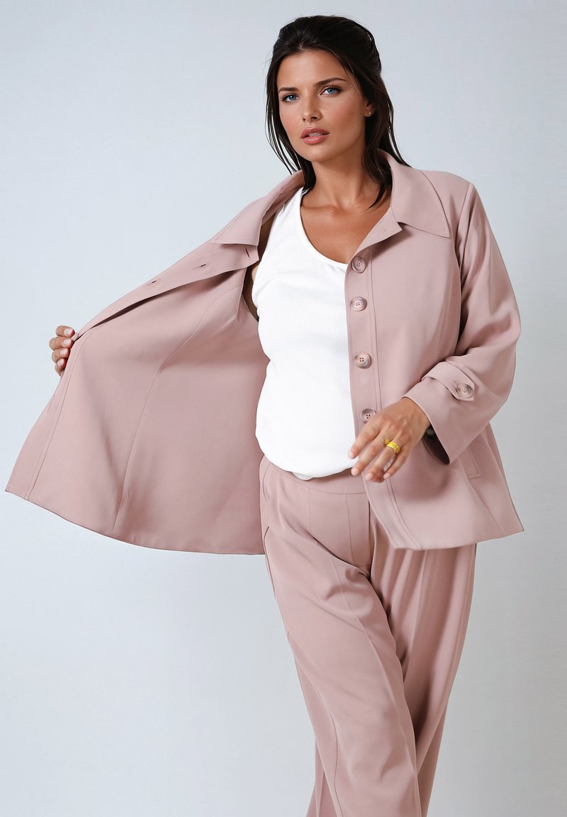 Light pink blazer with large front buttons, paired with a white tank top and matching pants, featuring a smooth fabric and relaxed fit.