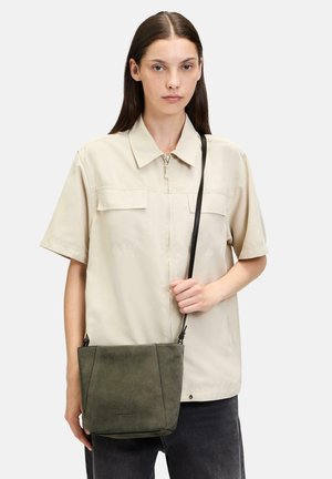 Grüne Wildleder-Crossbody-Tasche in rechteckiger Form, mit verstellbarem Ledergurt und subtiler Markenkennzeichnung am Boden.