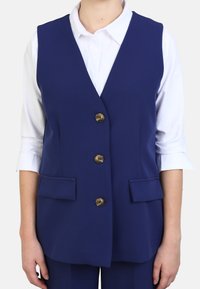 Marineblauer Weste mit V-Ausschnitt, taillierter Passform, fünf metallischen Knöpfen und zwei vorderen Taschen, über einem weißen Hemd getragen.