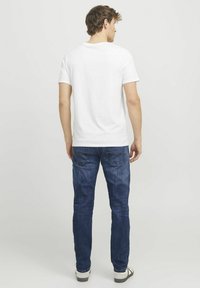 Weißes Kurzarm-T-Shirt, kombiniert mit blauen Jeans. Der Rücken des T-Shirts hat einen runden Ausschnitt und eine glatte Textur. Die Jeans haben Gesäßtaschen.