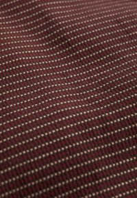 Detailní záběr texturované látky s malým kostkovaným vzorem v tmavě červené, vínové a světle béžové barvě.