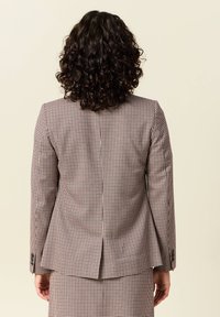 Ruudullinen bleiseri ruskean ja kermaan sävyissä, sopivan muotoinen ja takana yksi halkio, viimeistelty napitettujen hihansuiden kanssa.