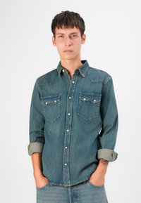 Blaues Denimhemd mit zwei Brusttaschen, Knopfleiste und aufgerollten Ärmeln. Verfügt über eine einfarbige Ausführung und ein klassisches Western-Stil Yoke-Design.