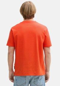 Orange t-shirt med korte ærmer og struktureret overflade, med rund halsudskæring og ensfarvet ryg, parret med lyseblå denim jeans.