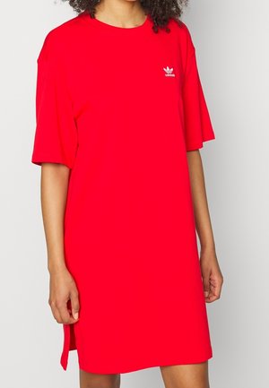 Personne portant une robe T-shirt Adidas rouge vif à manches courtes avec un petit logo Adidas blanc sur la poitrine.