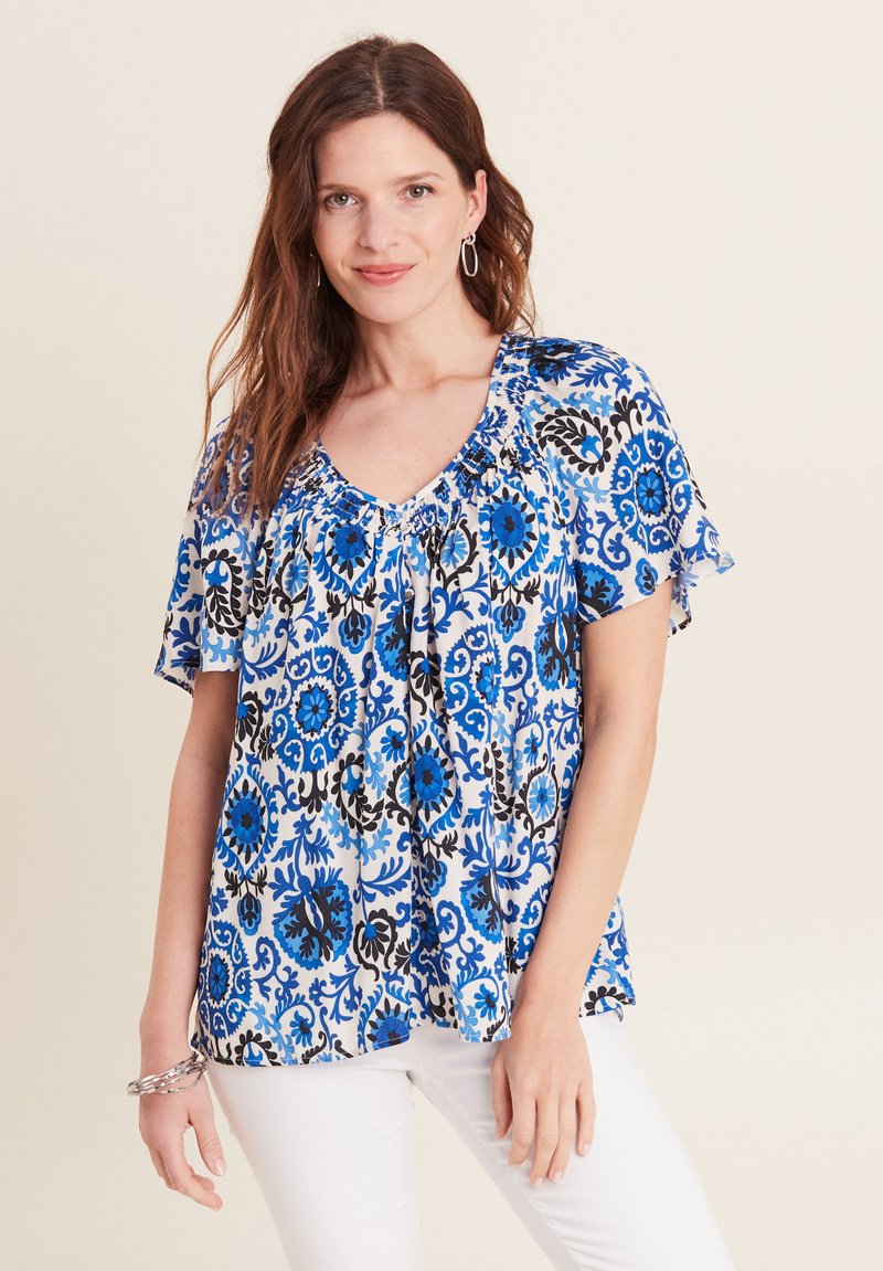 Blaues Blumenblusenshirt mit kurzen, schwingenden Ärmeln, das über einen dekorativen, gerafften Halsauschnitt und komplexe schwarze und blaue Muster auf hellem Grund verfügt.