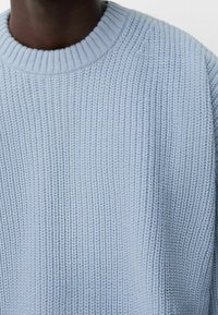 Pull tricoté bleu clair avec un design côtelé texturé et un col rond. Le tissu semble doux avec des coutures prononcées.