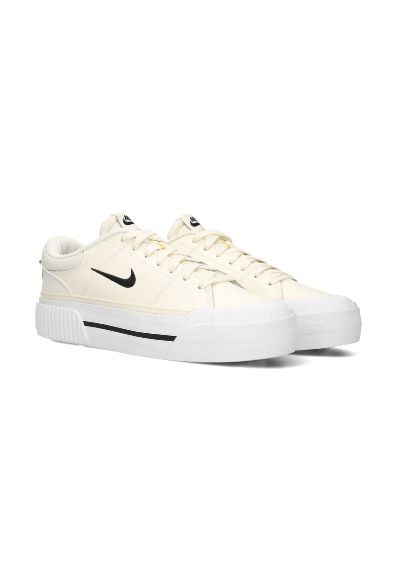 Zapatillas Nike en crema claro con parte superior de lienzo texturizado, logo Swoosh negro, suela de goma blanca y franja negra contrastante en la entresuela.