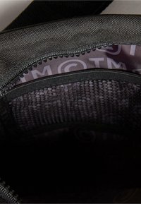 Sort rygsæks indvendighed med en struktureret mesh-lomme. Foringen har et subtilt mønster med branding-elementer og en glat lynlås.