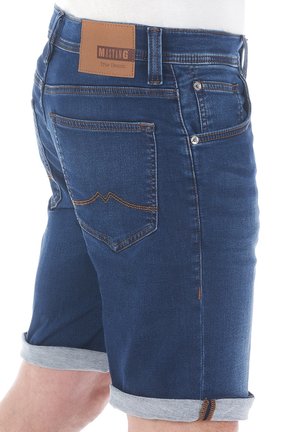 Shorts in denim blu scuro, con orli arrotolati, cuciture in contrasto beige e una patch in pelle con "MUSTANG True Denim" sul retro.
