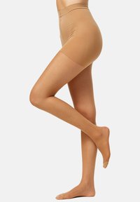 Pantalones cortos moldeadores de talle alto en color beige, con una textura suave, que presentan un diseño sin costuras y un acabado ligeramente transparente cerca de las aberturas de las piernas.