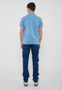 Polo shirt azzurro chiaro con maniche corte e colletto, abbinato a jeans blu scuro. L'outfit presenta dettagli azzurri chiari in contrasto.