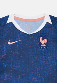 Francia nemzeti csapat mez, kék alapú, texturált mintával, fehér gallérral és rózsaszín Nike logóval, valamint kakas emblémával.