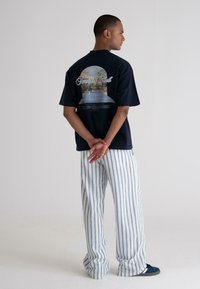 Navy graphic t-shirt with a design featuring a tennis court; paired with light blue and white striped wide-leg pants. Texture is smooth.